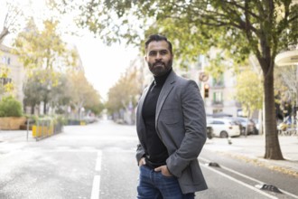 Stylish Indian businessman with a well-trimmed beard stands confidently on an urban street lined
