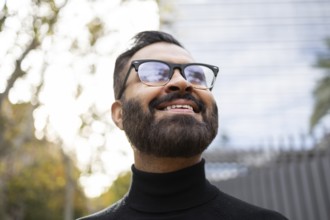 From below cheerful Indian businessman wearing sunglasses and a black turtleneck enjoys a sunny