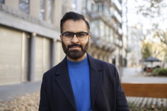 Indian businessman in a stylish winter outfit with a blue sweater and dark coat, standing outdoors,
