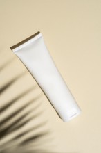 Top view of a minimalist designed cosmetic tube stands against a beige background, casting soft