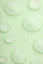 This image features a close-up view of translucent droplets scattered on a smooth, light green