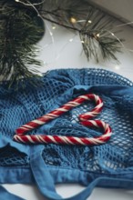 A blue string bag overflowing with red and white striped candy canes, placed alongside a pine