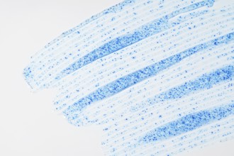 A close-up of face scrub smears showcases fine blue micro-exfoliating particles against a smooth