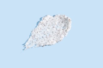 Exfoliating cream with microbeads smeared against a pale blue background, showcasing the texture