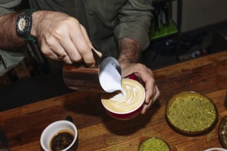 A barista delicately pours steamed milk into a latte, creating intricate latte art. The scene
