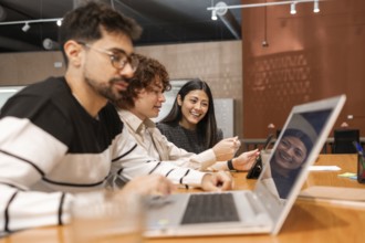 A group of diverse coworkers collaborating in a modern office setting, using laptops and tablets