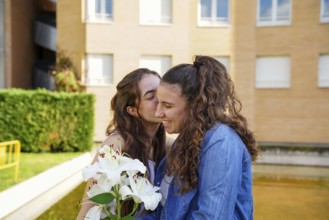 A young LGBTQ+ women couple, sharing a tender moment outside, with one women kissing the other on