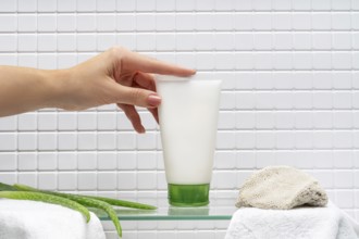 Cropped unrecognizable woman holding a tube of body care cream beside aloe gel in a bathroom, with
