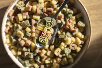 Top view of a metal spoon lifting colorful number shaped pasta from a bowl, clearly showing the