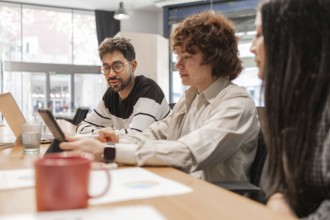 Three coworkers discuss projects around a wooden table in a bright, modern office They share ideas