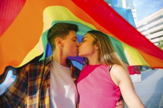 A joyful lesbian couple shares a tender moment under a vibrant rainbow flag, symbolizing pride and