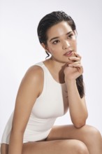 A fresh portrait of a young woman wearing a white bodysuit in a studio setting, gazing slightly