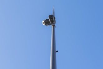Low-angle view of surveillance cameras mounted on a tall pole, set against a clear blue sky. The