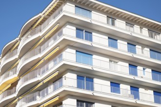 A modern apartment building features multiple curved balconies, white facade, and glass railings,