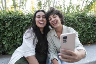 A cheerful lesbian couple takes a selfie with a smartphone in a garden. They smile brightly,