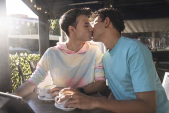 A loving gay couple shares a tender kiss while enjoying coffee at an outdoor cafe. Their connection