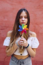 A teenage girl with long hair holds a vibrant pinwheel against a coral backdrop. She appears calm