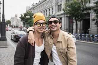 A joyful gay couple is embracing on a bustling city street, showcasing casual style and happiness.