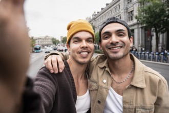 A Colombian gay couple smiling while taking a selfie outdoors, capturing an authentic, joyful