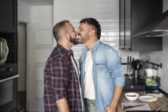 A joyful gay couple in a kitchen, playfully sharing cream from a dessert, showcasing love and