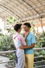 A cheerful gay couple embracing in a lush indoor garden. Their colorful outfits and vibrant