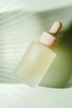 A frosted glass serum dropper bottle hovers against a blurred green background, depicting motion