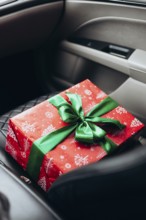 A beautifully wrapped red gift with a green ribbon rests on a car seat, capturing the anticipation
