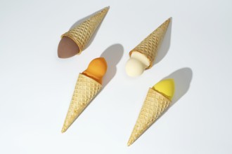 Four colorful cosmetic sponges creatively arranged in waffle cones, resembling ice cream scoops,