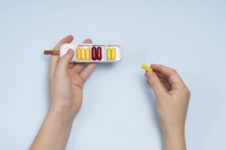 Top view of a cropped unrecognizable person's hand holding a white pill box filled with colorful