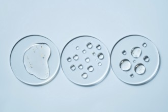 Three transparent petri dishes with water droplets placed on a light blue surface The circular