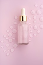 A clear glass dropper bottle on a pink background, surrounded by scattered water drops The scene
