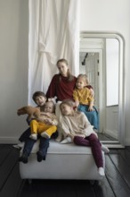 Five children, dressed in vibrant outfits, sit and play together in a cozy room with a large mirror