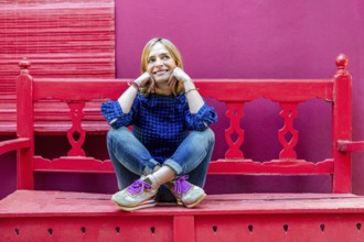 A woman wearing a blue plaid shirt sits cross-legged on red wooden stairs, smiling gently and