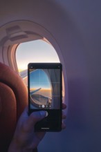 Cropped unrecognizable person capturing a serene sunset through an airplane window using a