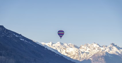 A vibrant hot air balloon floats gracefully over the Swiss Alps, showcasing a panorama of snow-clad