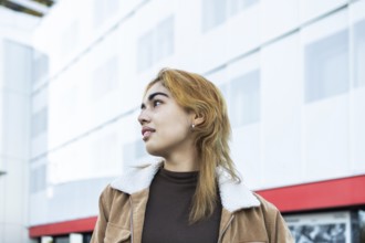 A Mixed-race woman with light hair and a stylish jacket gazes to the side, set against a modern
