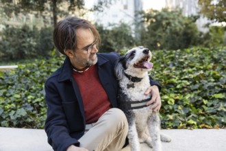 A middle-aged man interacts with his black and white dog in a city park, surrounded by lush