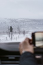 A hand captures a snowy landscape from inside a vehicle, showcasing the tranquil and harsh beauty