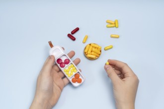 From above cropped unrecognizable hands hold a pill box and select different colored capsules and