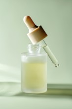 A translucent serum dropper bottle with a single drop hanging from the pipette, showcased against a