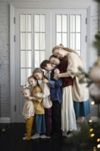 A loving family of six embraces warmly in front of a white-paneled doorway Their cozy clothing and