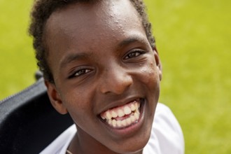 Joyful close-up of a smiling boy with cerebral palsy at surf camp, enjoying a bright sunny day. The