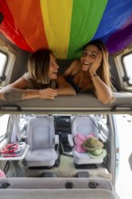 Lesbian couple are happily relaxing inside a camper van adorned with a rainbow flag, symbolizing