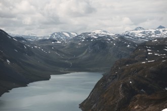 A sweeping view of a tranquil lake nestled in a dramatic mountain valley in Norway Snow-dusted