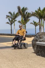 A man in a wheelchair is captured enjoying the sunny weather on a paved path. He is dressed in a