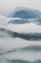 A peaceful lake reflects layers of mist and towering mountains in Norway The hazy atmosphere and