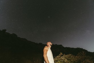 A man gazes upwards, immersed in the wonder of a star-filled night sky The serene landscape and