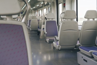 A spacious and well lit interior of a modern train, featuring rows of empty gray seats and purple.