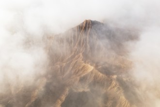 A breathtaking mountain peak emerges through a dense layer of clouds, showcasing its rugged terrain