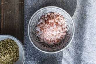 Close-up of Himalayan pink salt in a decorative ceramic bowl alongside fresh green herbs on a